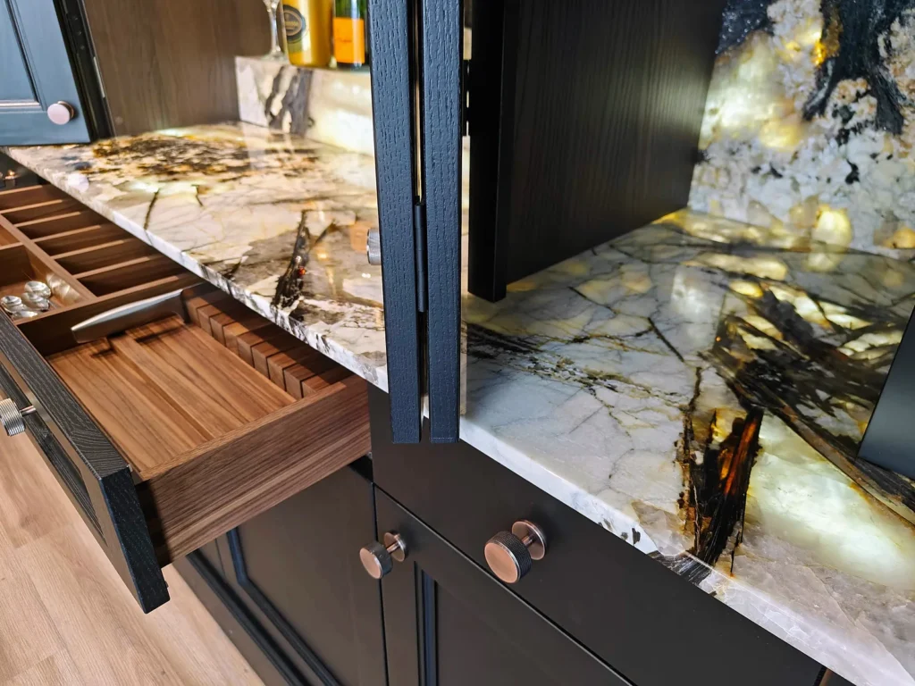 Backlit natural stone worktop and splashback with walnut cutlery and knife inserts in black in-frame cabinetry, by Kraus Kitchens
