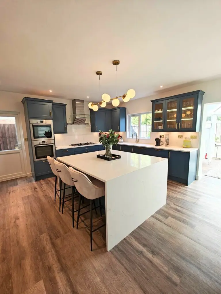 Navy blue kitchen island with bar seating, waterfall quartz worktop and brass globe pendant lights, Bromley